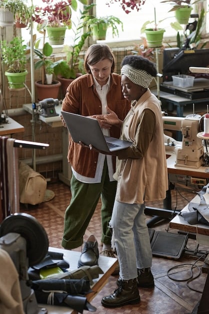A diverse group of small business owners gathered around a table, collaborating on laptops and discussing application strategies. The setting is a coworking space with modern design.